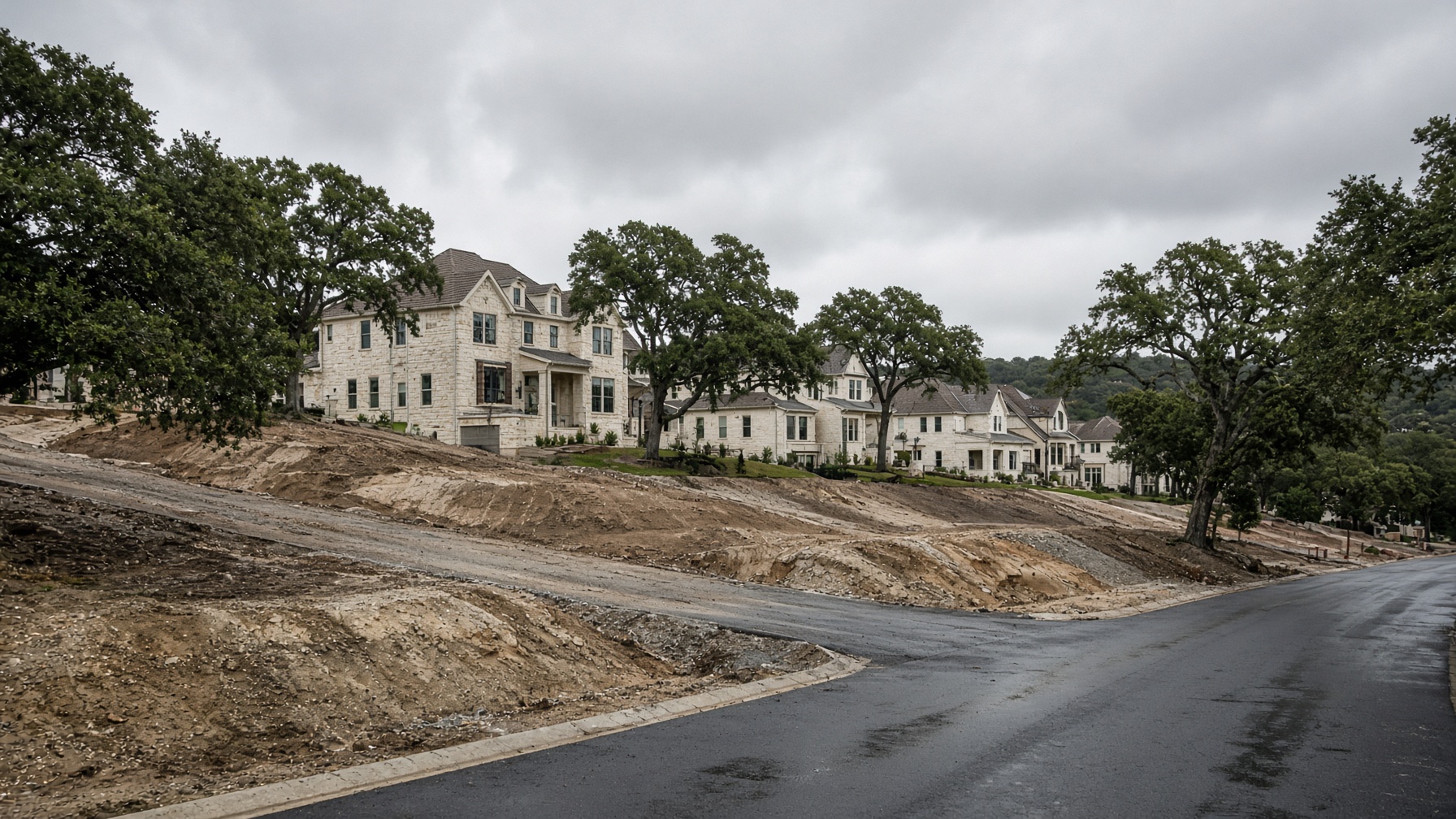 Hillside new-construction neighborhood in Leander, Texas after rain, limestone homes stepping down a slope.
